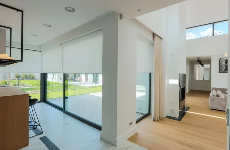 Auf dem Bild ist ein großes, lichtdurchflutetes Wohnzimmer mit großen Fensterfronten zu sehen, die mit Rollos von Suntec aus Coesfeld gegen die Sonne geschützt sind.